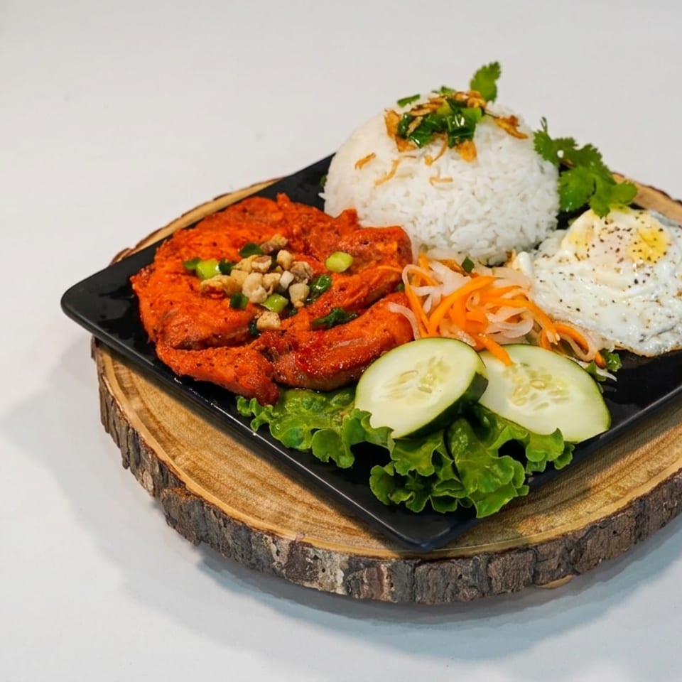 Plated meal with red curry, rice, fried egg, pickled vegetables, cucumber, and lettuce on a wooden serving board.