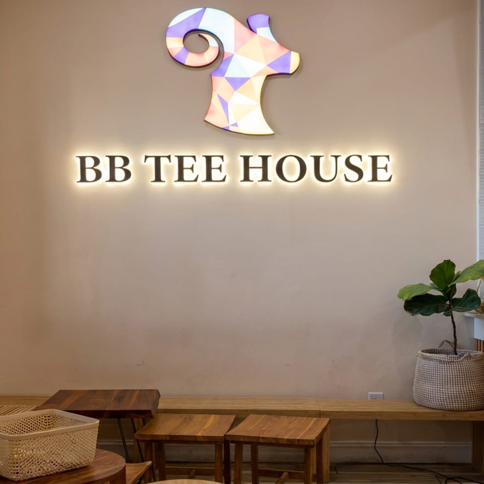 BB Tee House reception area with illuminated signage, Vietnamese bánh mì menu screens, plants, and wooden seating.