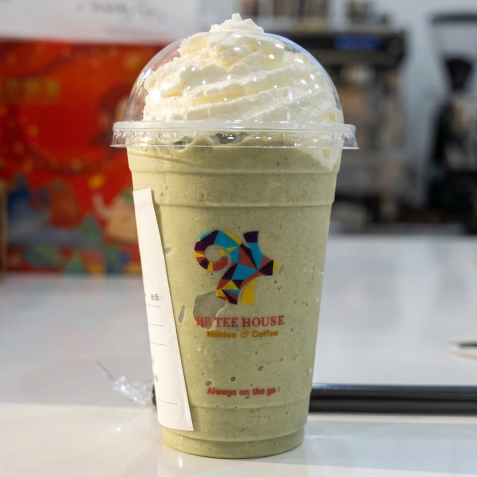 Green matcha smoothie topped with whipped cream in a branded plastic cup on a café counter.