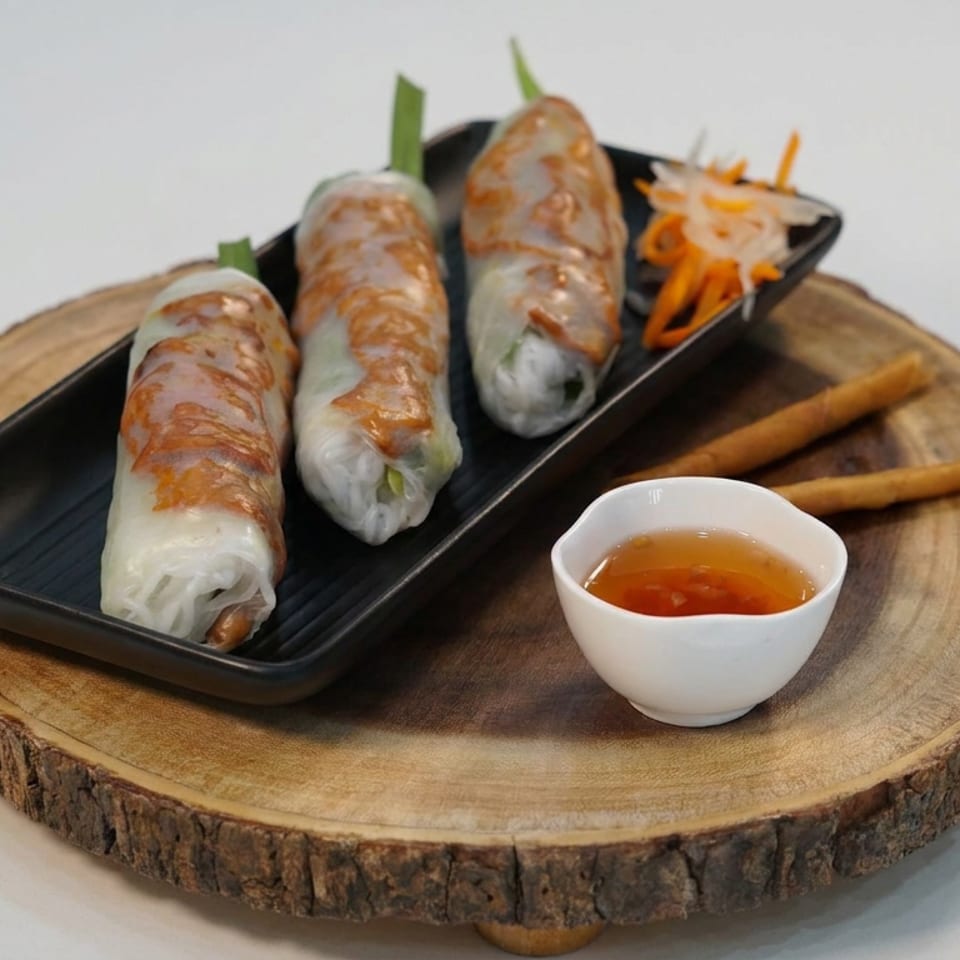 Three fresh Vietnamese spring rolls on a black plate with dipping sauce, chopsticks, and shredded vegetables on a wooden serving board.
